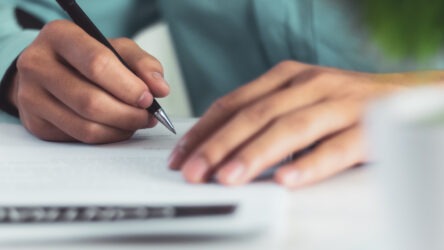 A close-up of a man’s hands filling out Form DS-230.