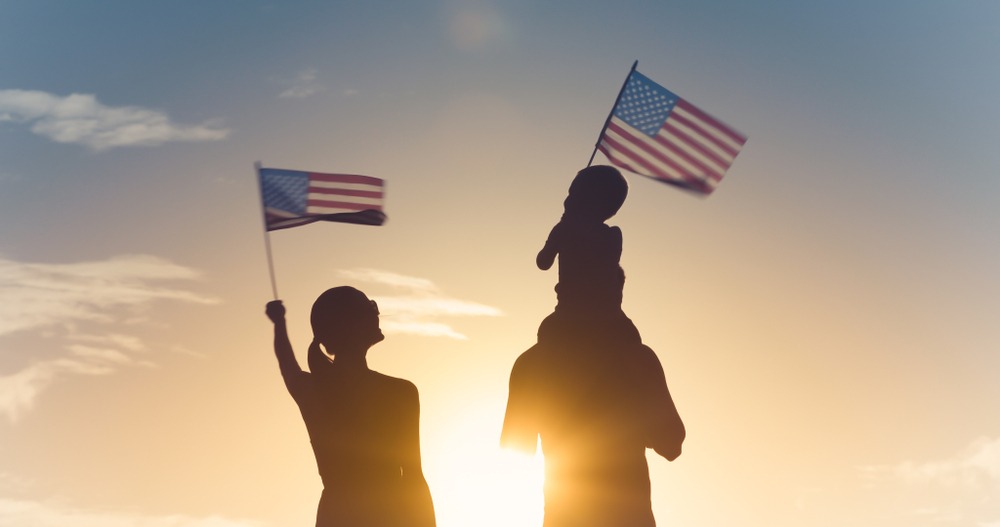 Silhouette of family waving USA flags. How long does it take USCIS to process marriage green cards?