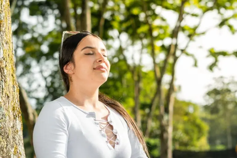 Woman standing near some trees with her eyes closed