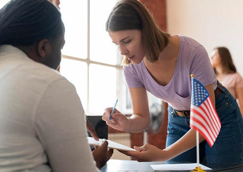 Woman signing a document with an American flag sitting on a desk
